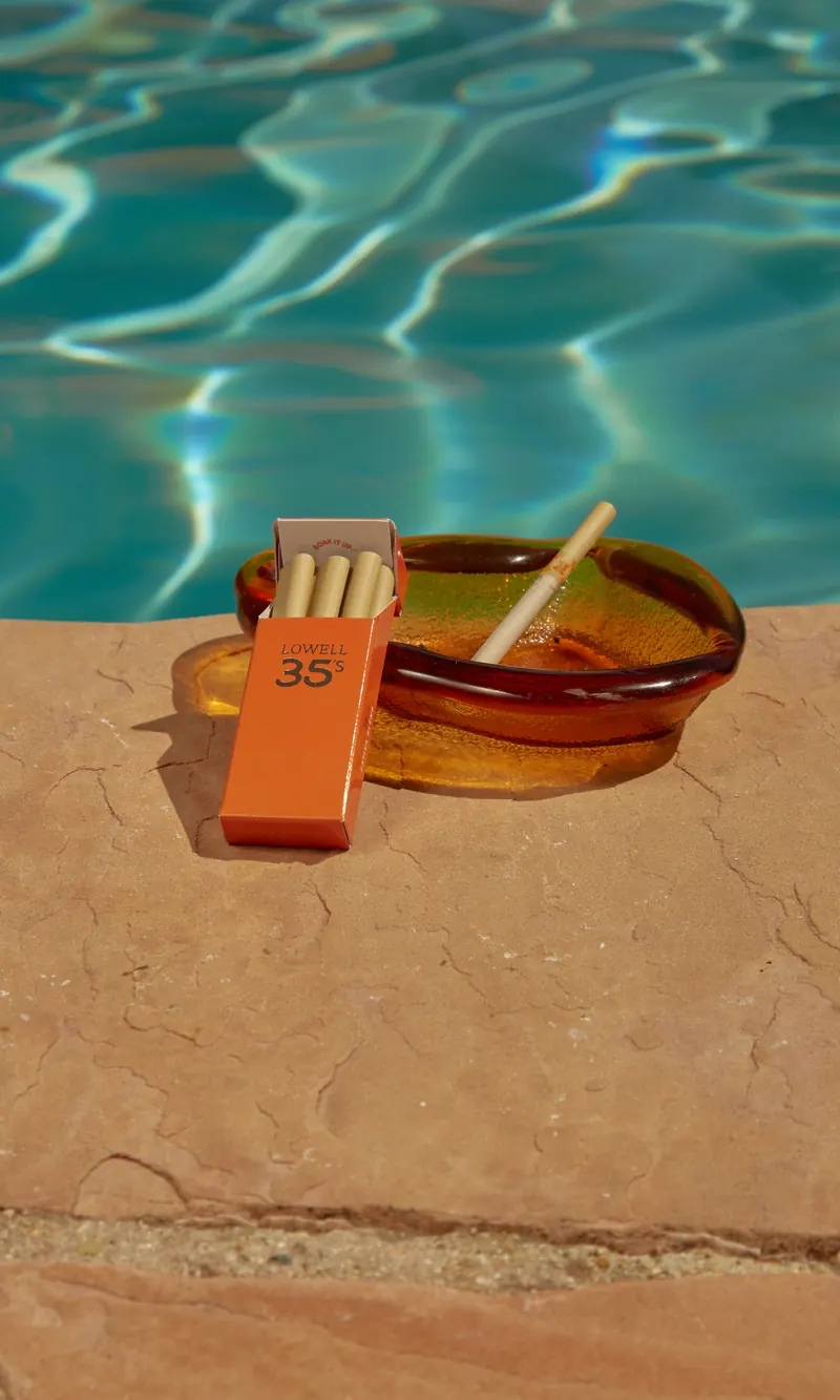 A pack of Lowell 35's and an amber ashtray on the edge of a pool
