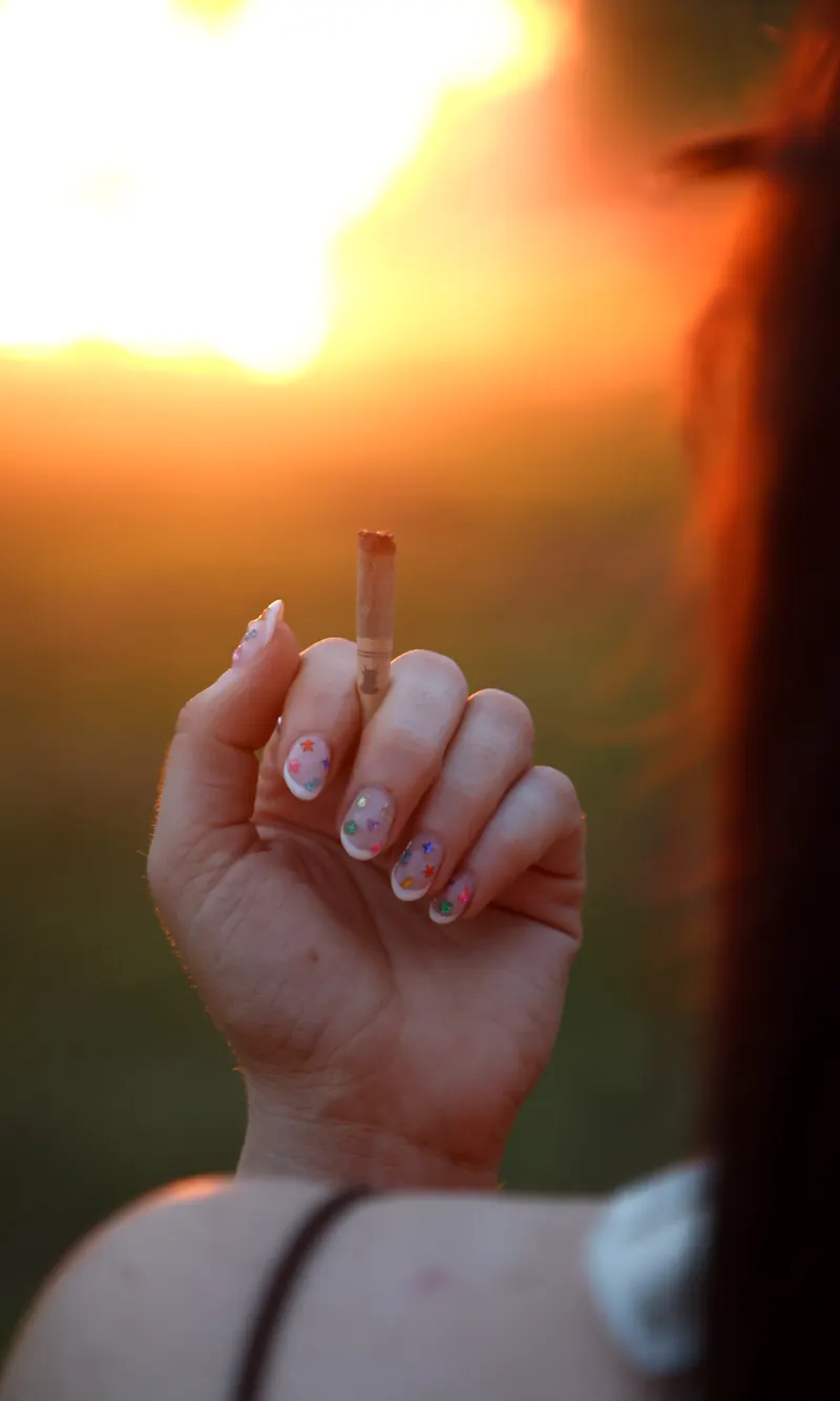 A hand holding up a lit pre-roll against a low sun